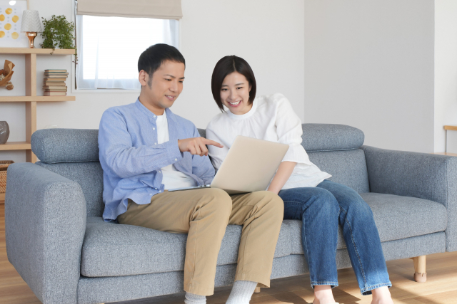 ソファーに座ってノートパソコンを使う夫婦